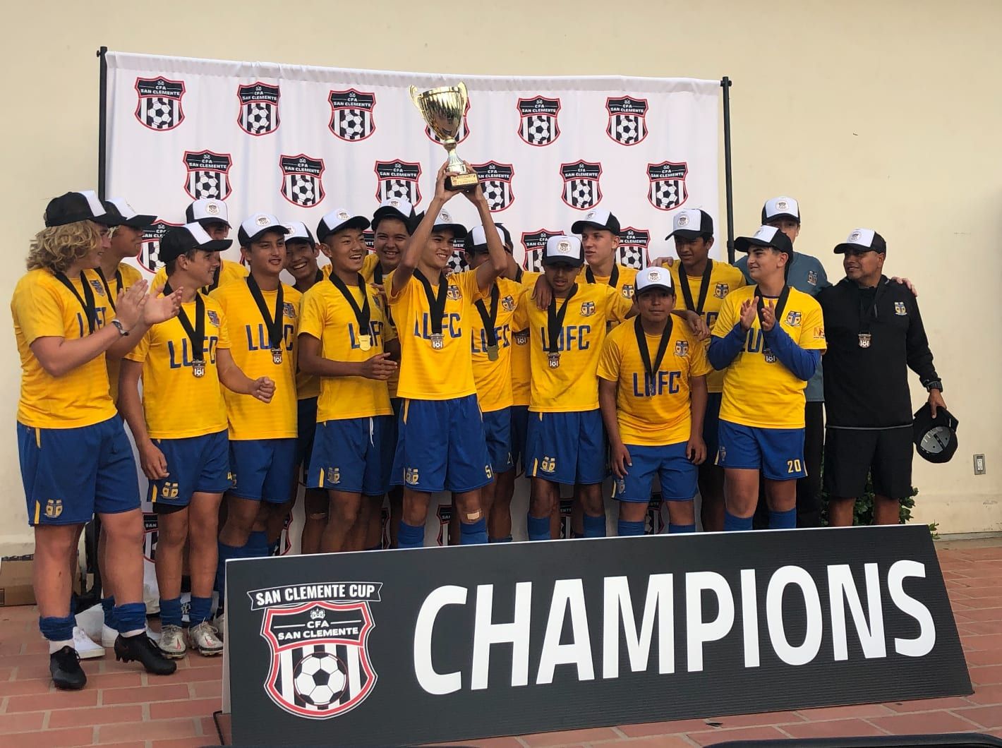 Boys champions in yellow raising the San Clemente Cup trophy