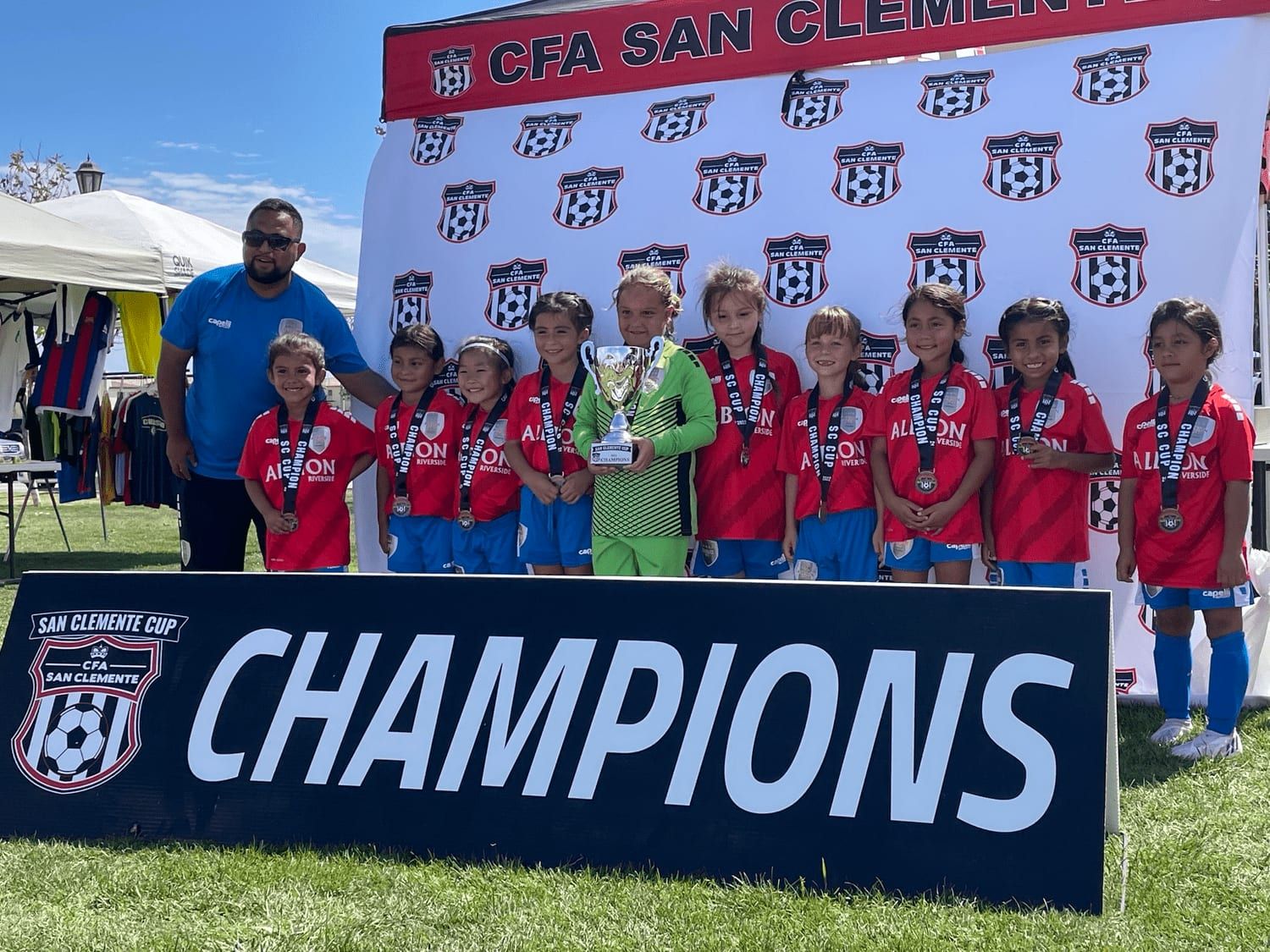 Girls champions in red with their trophy behind the champions banner