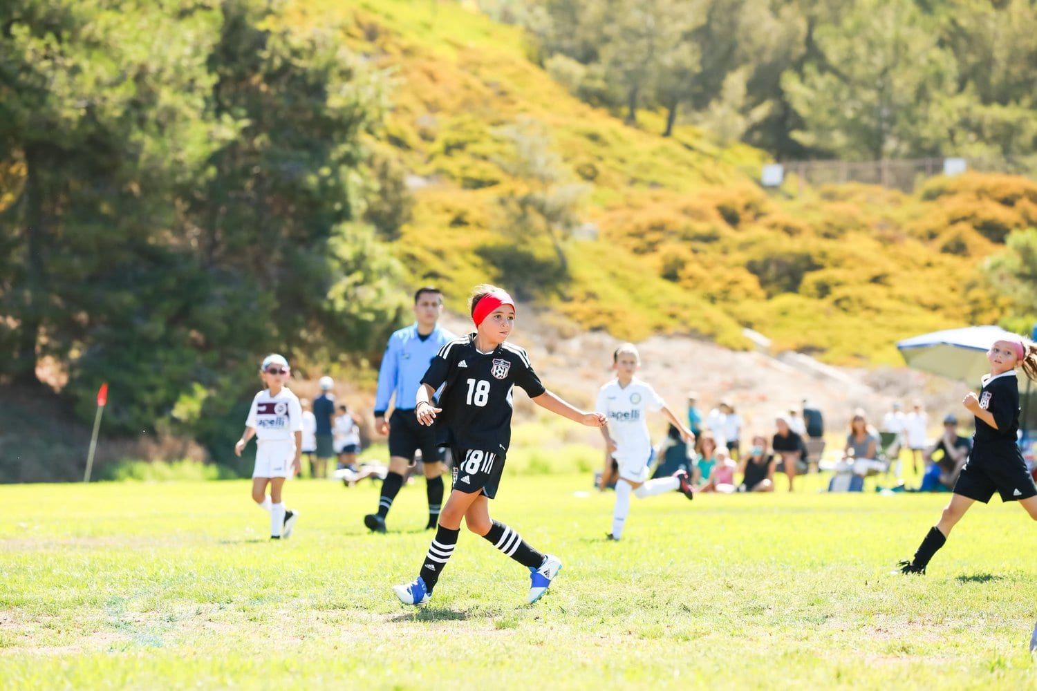 Young boys player in black running onto the ball below a coastal hillside